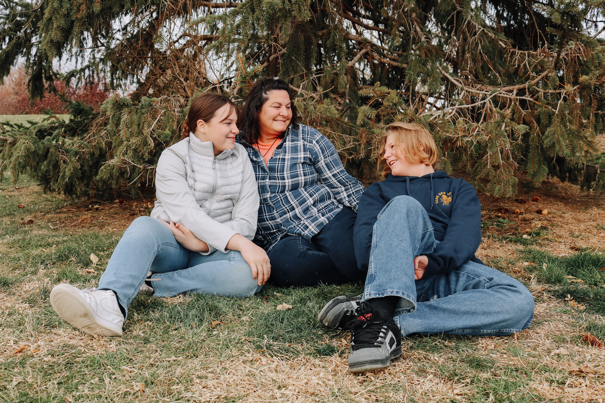 Family of three sitting on grass, looking happily at each other