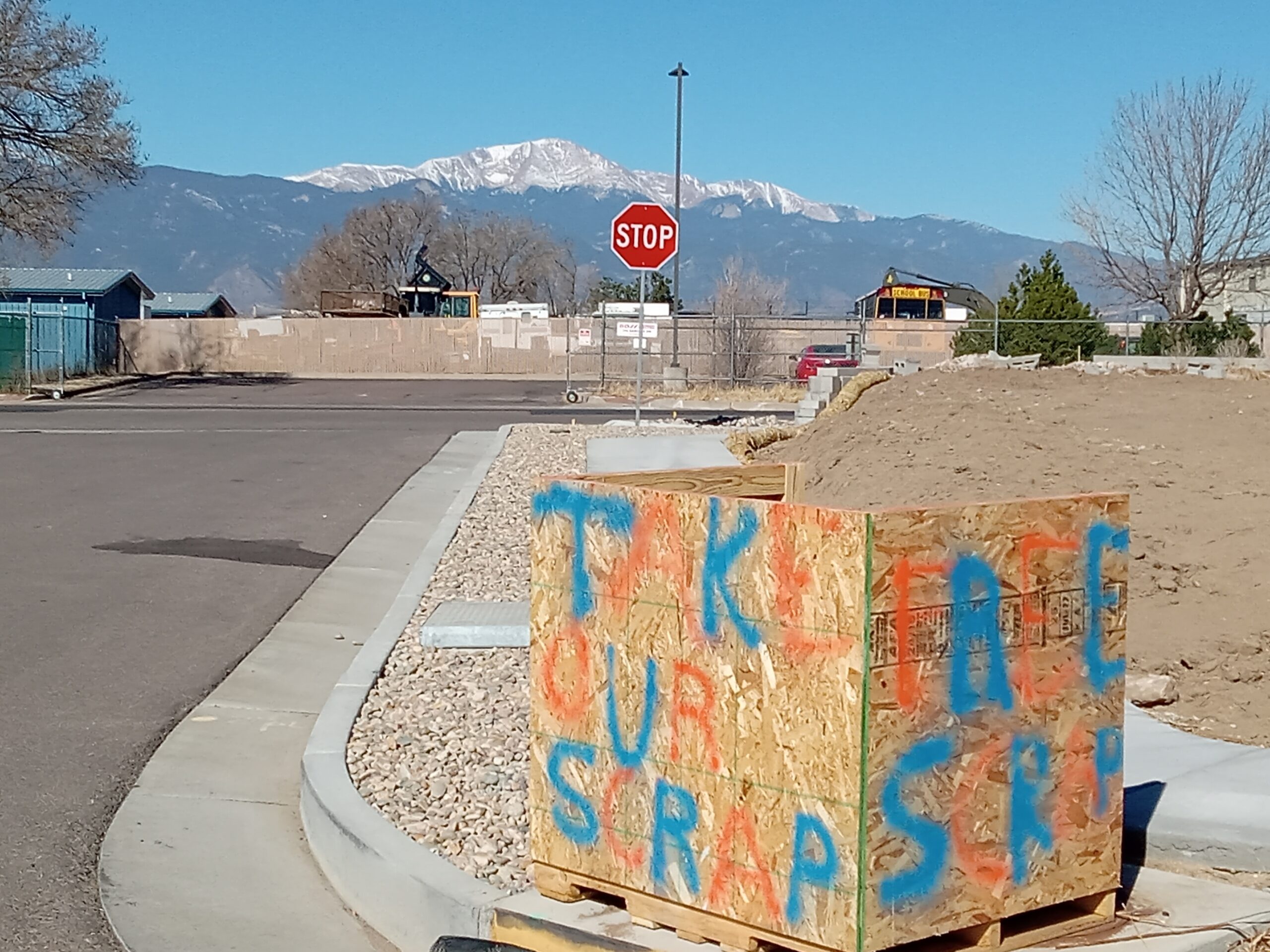 Wooden box that says "Take our scrap," with Pikes Peak in the background