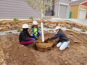 Volunteers kneeling around the base of a tree in front of a new home.