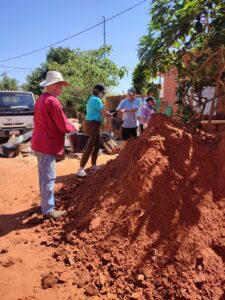 Volunteers stand by a pile of red dirt.