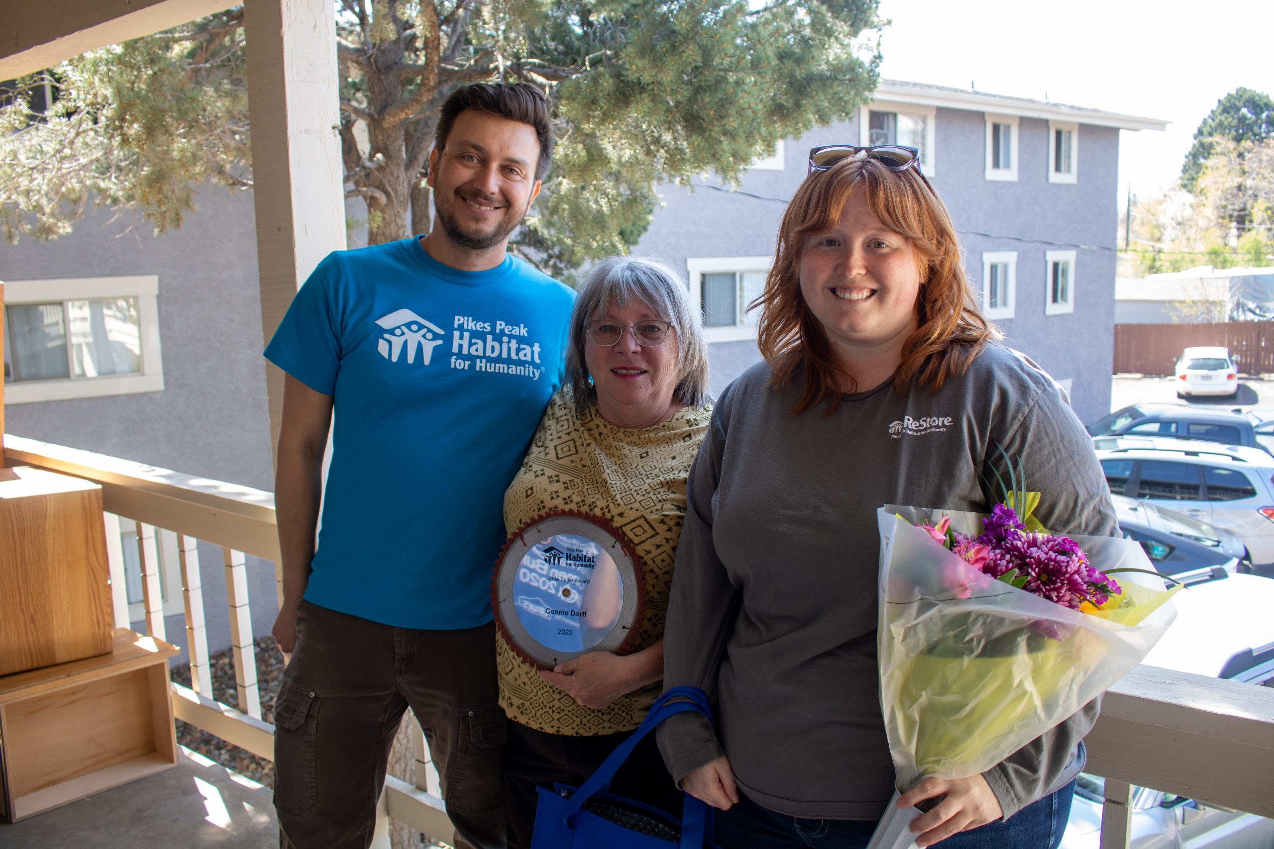 Three people standing on a patio with awards and flowers