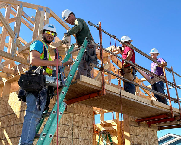 A man wearing a construction hat smiles while standing on a ladder with three other volunteers on a scaffolding