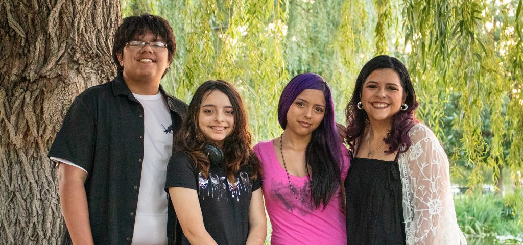 A son, two daughters, and a mother pose in front of overhanging branches of a tree
